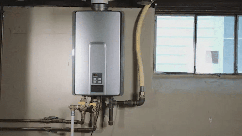 Wall-mounted tankless water heater with pipes beside a window in a utility room