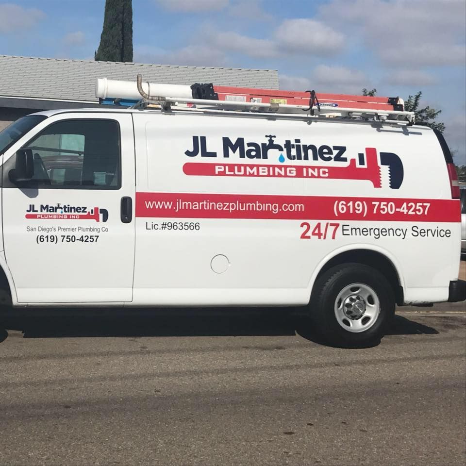 White JL Martinez Plumbing service van with ladder rack parked outdoors, showing company logo and phone number.