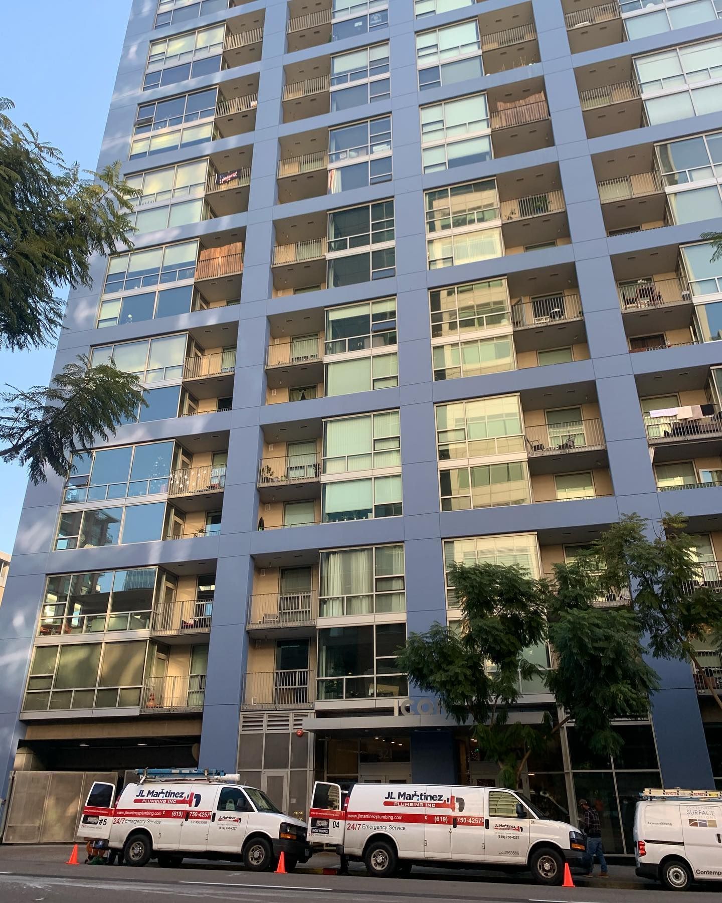 Tall apartment building with glass balconies and parked service vans on the street below