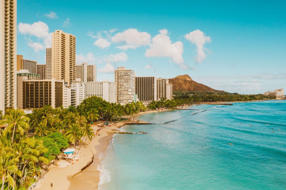 High-rise hotels beside a palm-lined beach and turquoise ocean under a blue sky