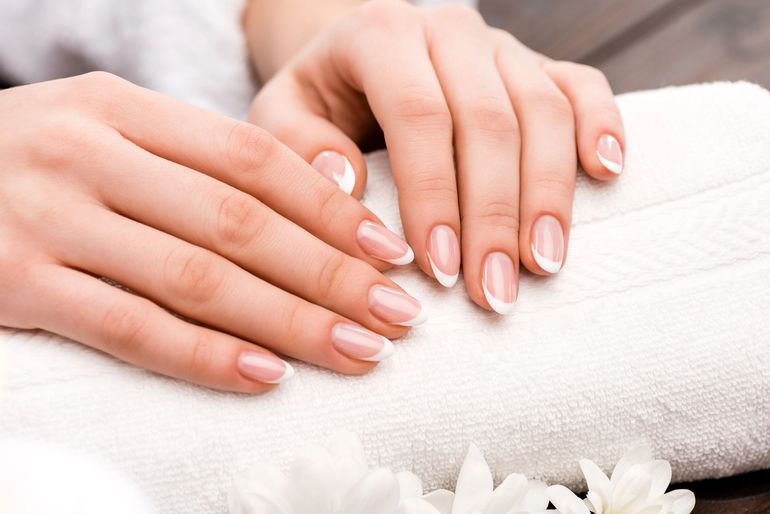 Mani con unghie curate color rosa pallido appoggiate su un asciugamano bianco.