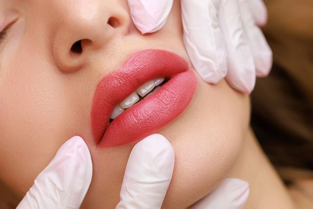 Primo piano di labbra toccate con mani guantate, che mostra un trattamento cosmetico alle labbra.