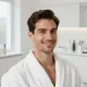 Uomo sorridente in accappatoio bianco in un bagno luminoso