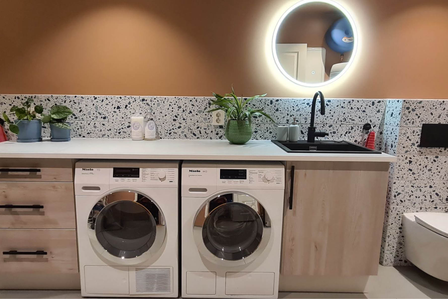 Etterbilde av nytt vaskerom, med stor benk med svart servant, tørketrommel og vaskemaskin under benken.
