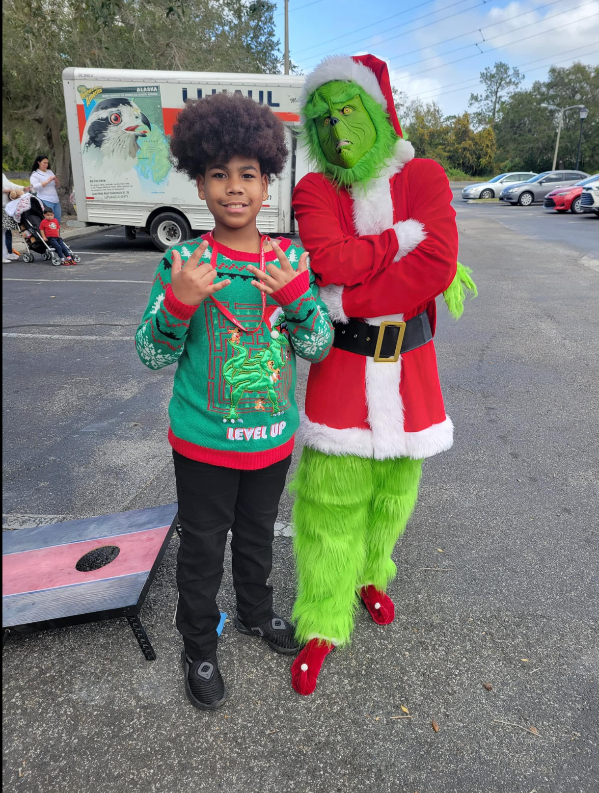 A boy is standing next to a grinch mascot in a parking lot.