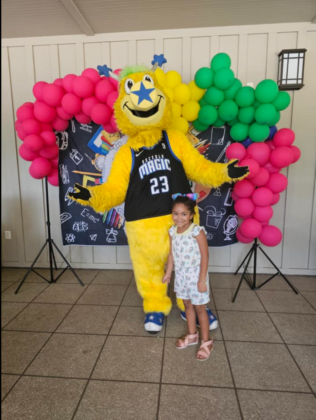 A little girl stands next to a mascot wearing a magic jersey