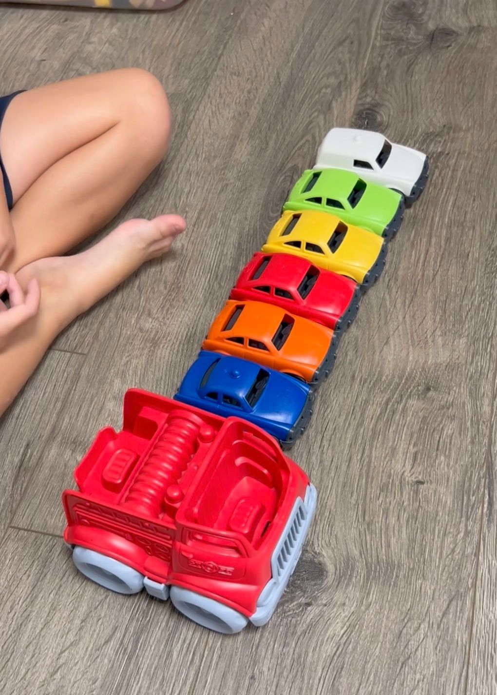 A child is playing with a row of toy cars on the floor