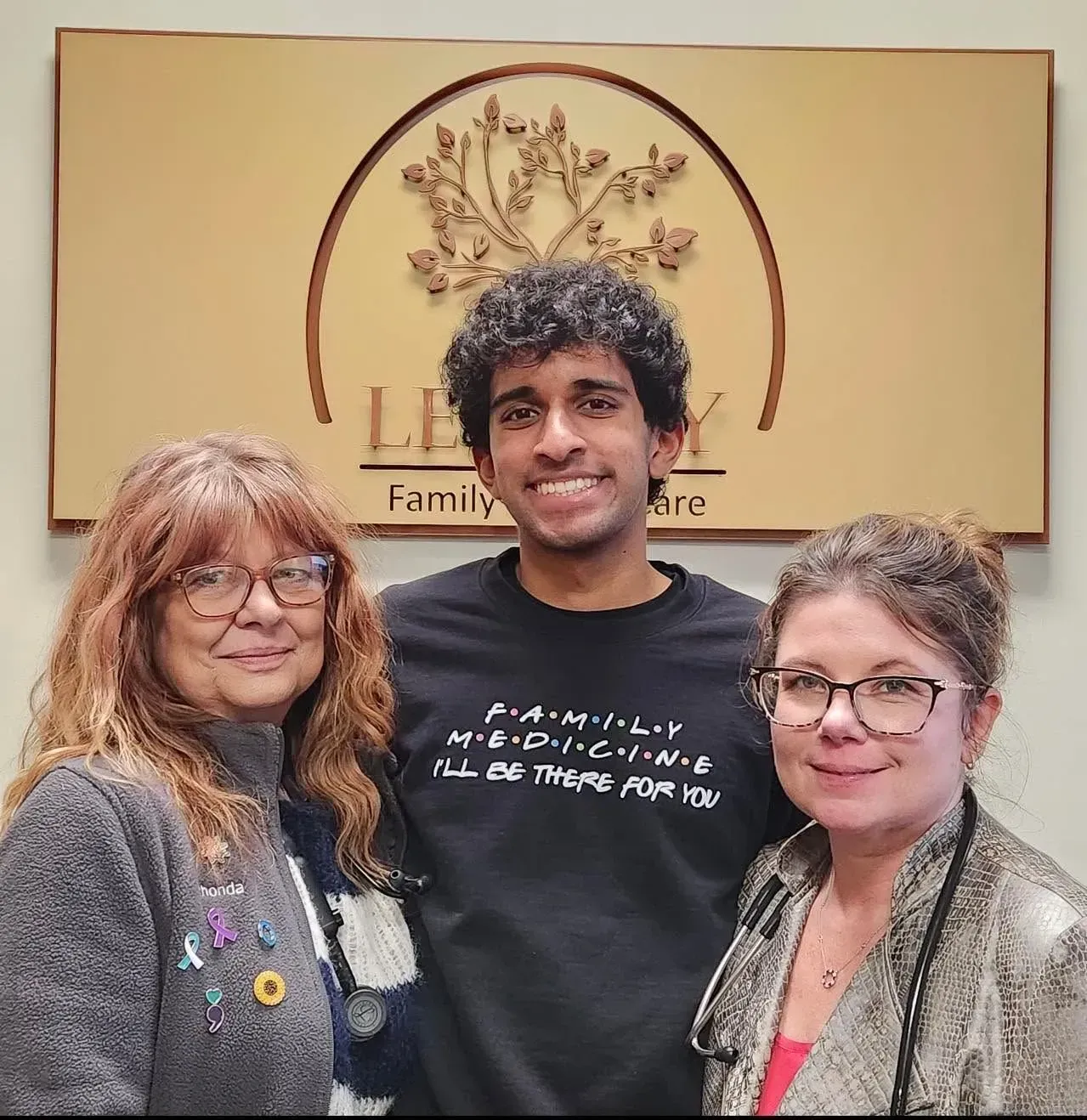 Three people smiling indoors in front of a family service sign