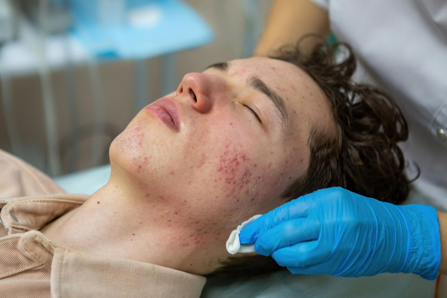 Gloved hand applying skincare product to a reclining person’s cheek in a clinic setting