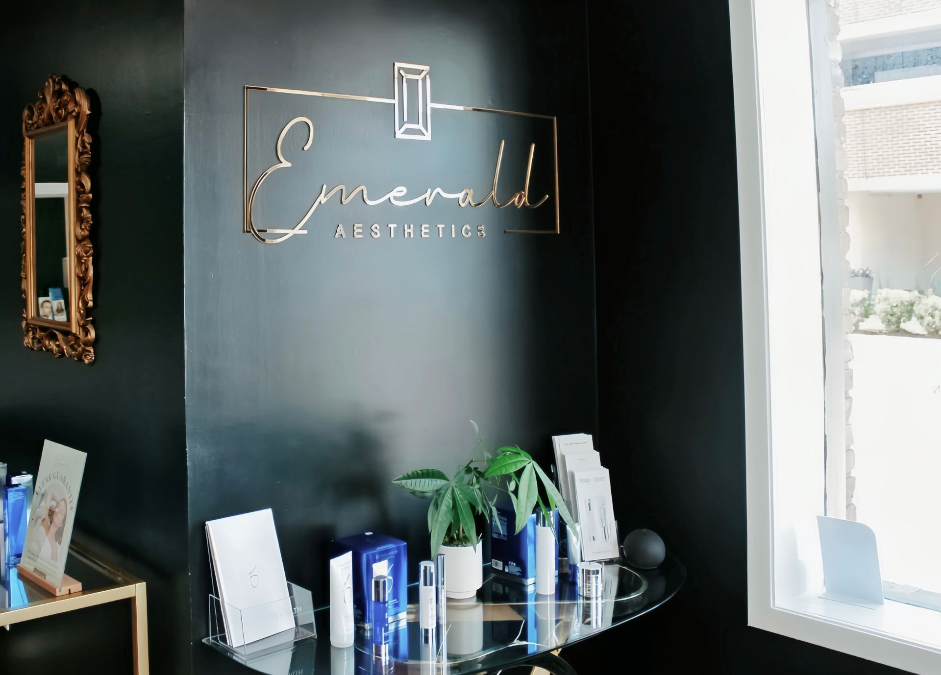 Interior of an “Emerald” salon reception area with a black wall, glass table, and brochures near a window