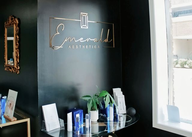 Interior of an “Emerald” salon reception area with a black wall, glass table, and brochures near a window