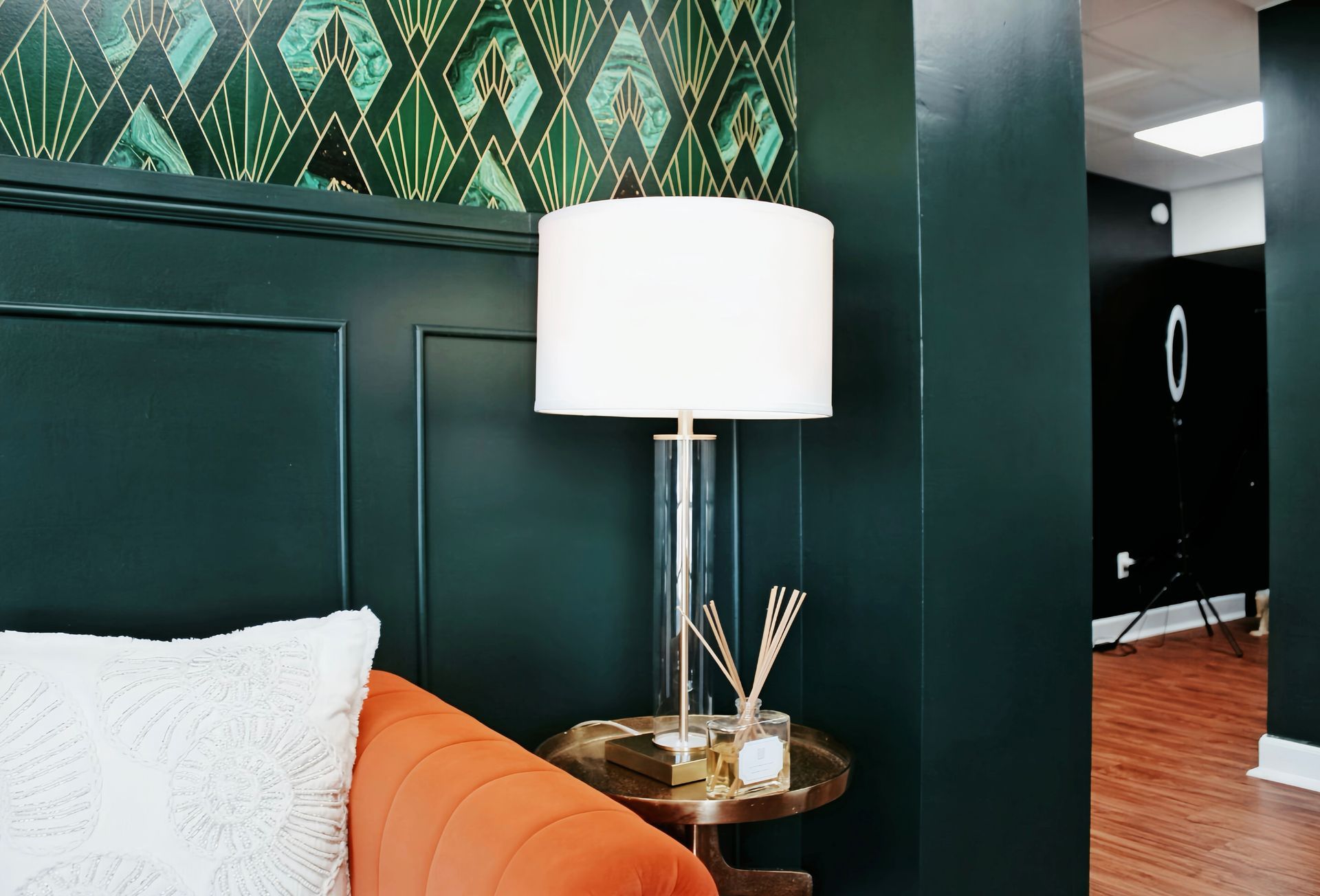 Teal hotel room corner with orange chair, white lamp, and dark green wall paneling