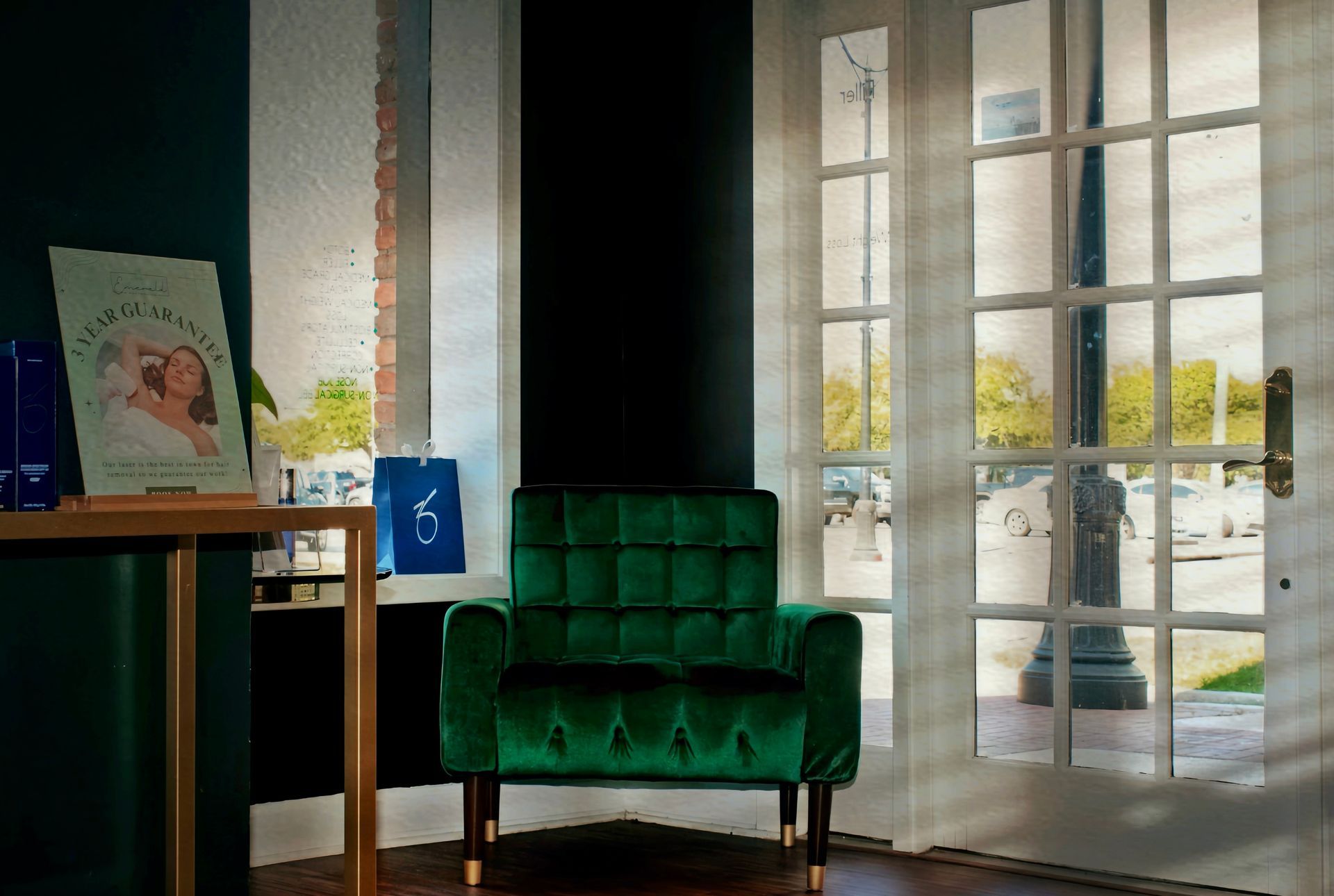 Green velvet chair by a sunlit window in a modern room with a small table and framed art.