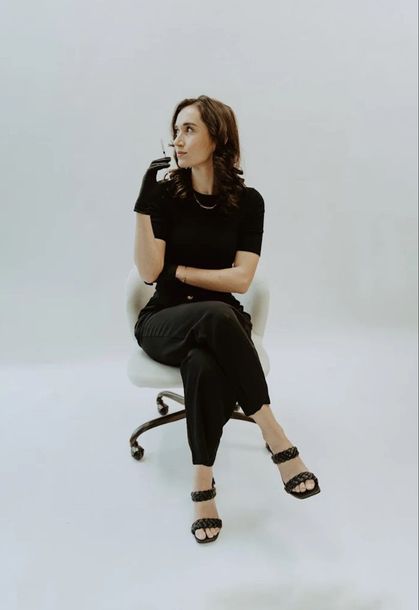 A woman in a black shirt and black pants is sitting in an office chair.