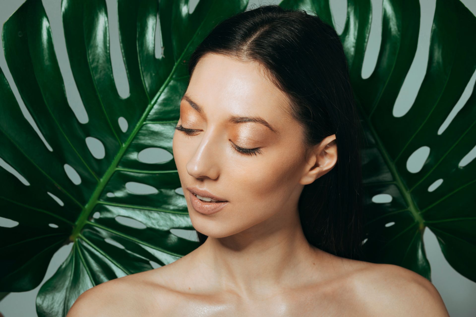 Woman with closed eyes among lush green tropical leaves
