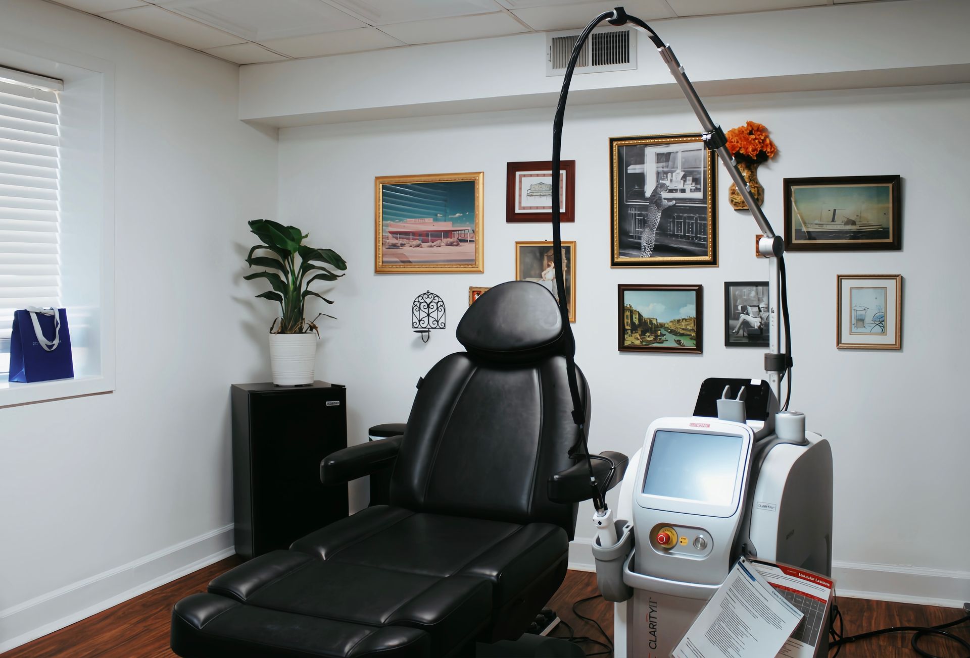 Home treatment room with black reclining chair, artwork on white walls, and medical equipment.