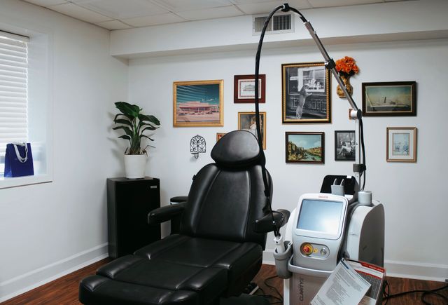 Home treatment room with black reclining chair, artwork on white walls, and medical equipment.