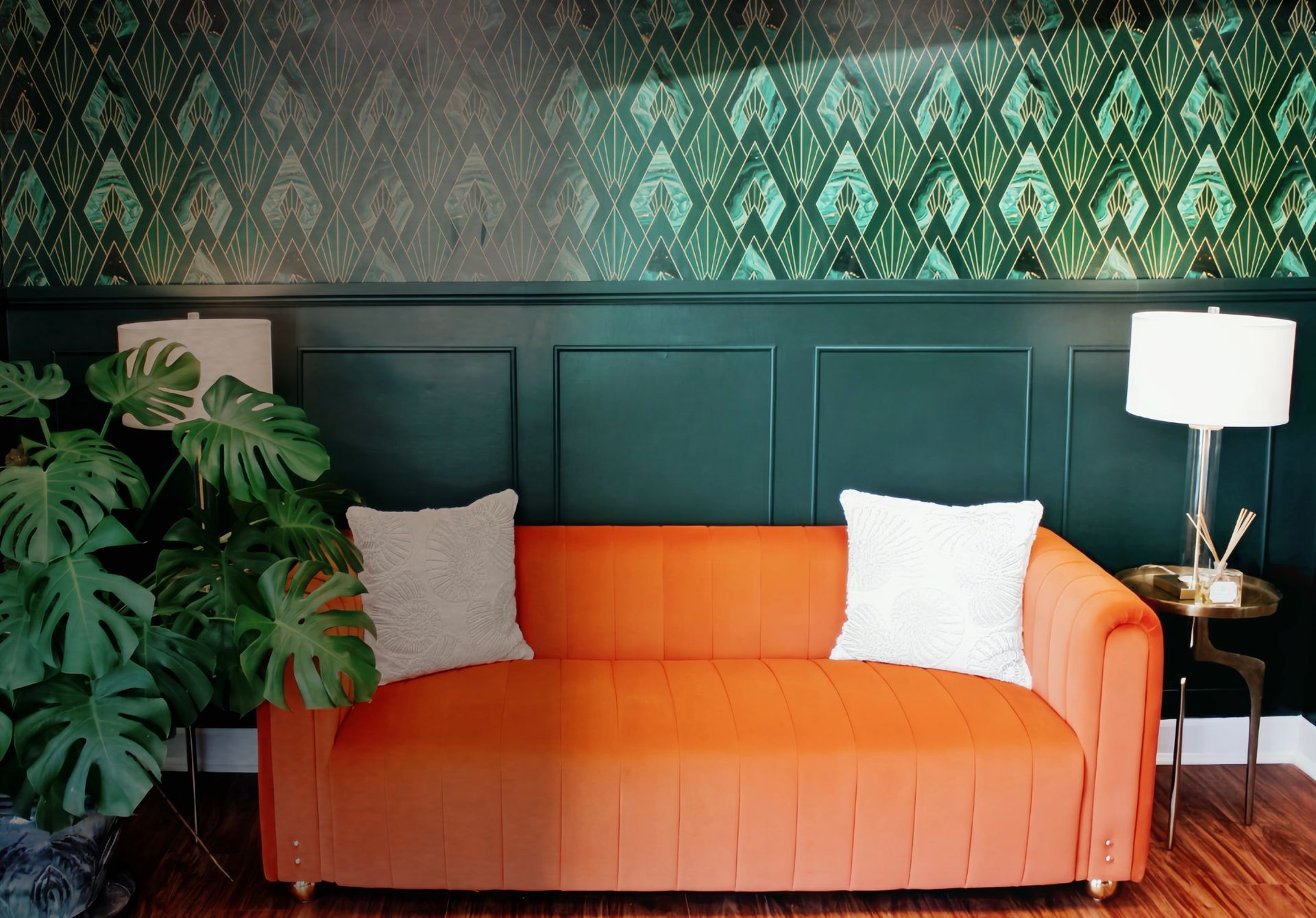 Orange sofa with white pillows in a green-paneled living room beside a lamp and large plant