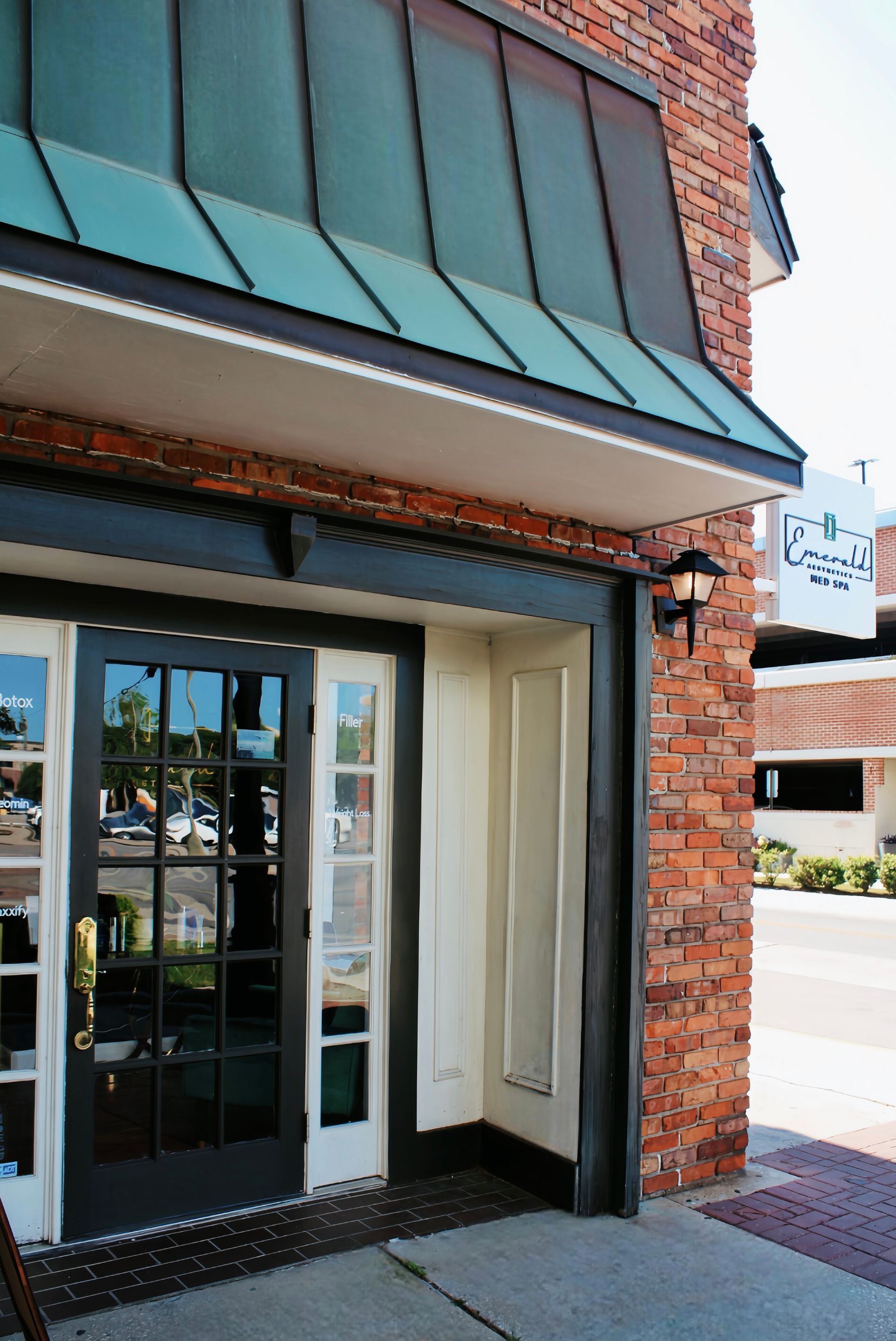 Brick storefront entrance with teal awning, glass double doors, and sidewalk outside