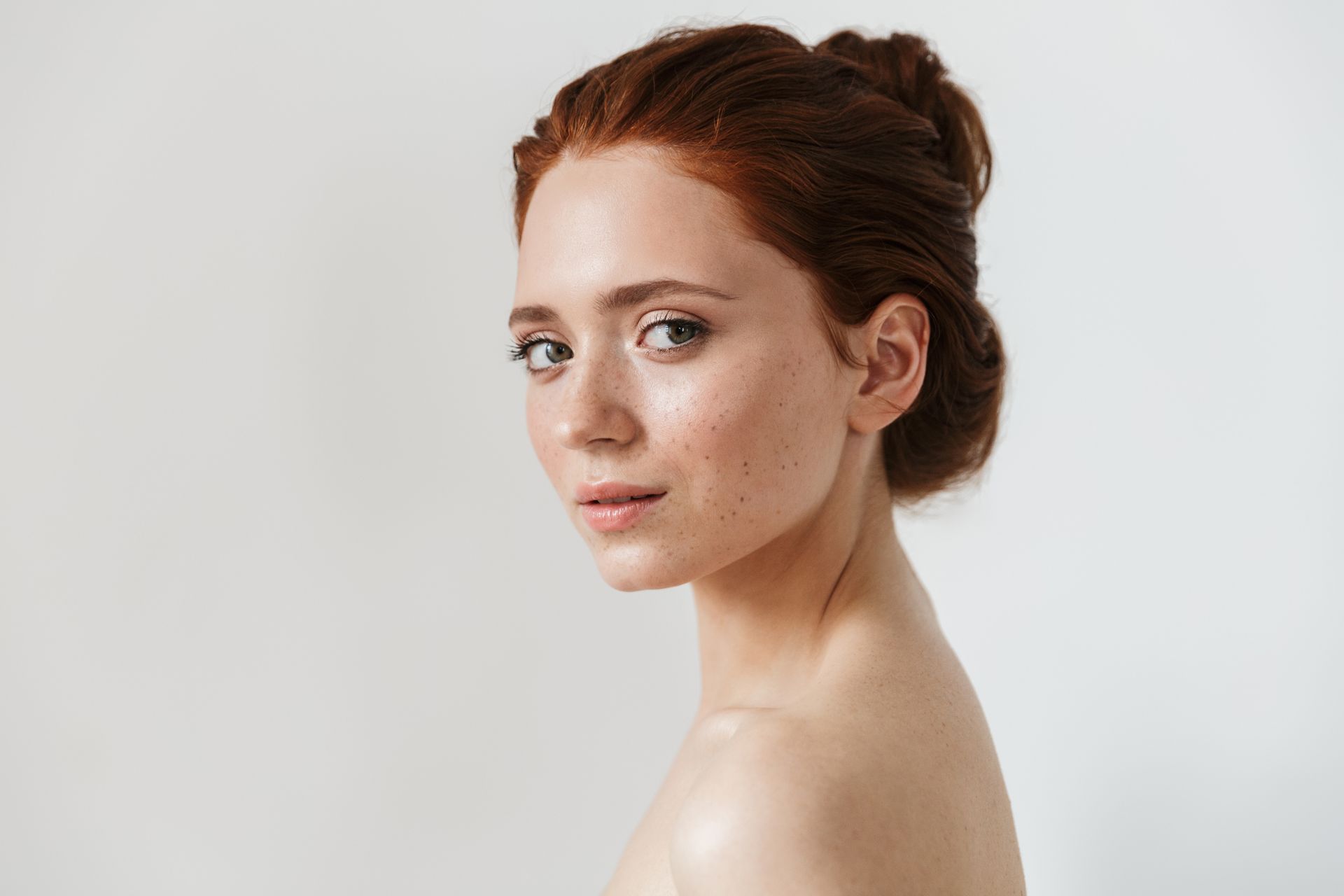 A woman with red hair and freckles is looking over her shoulder at the camera.