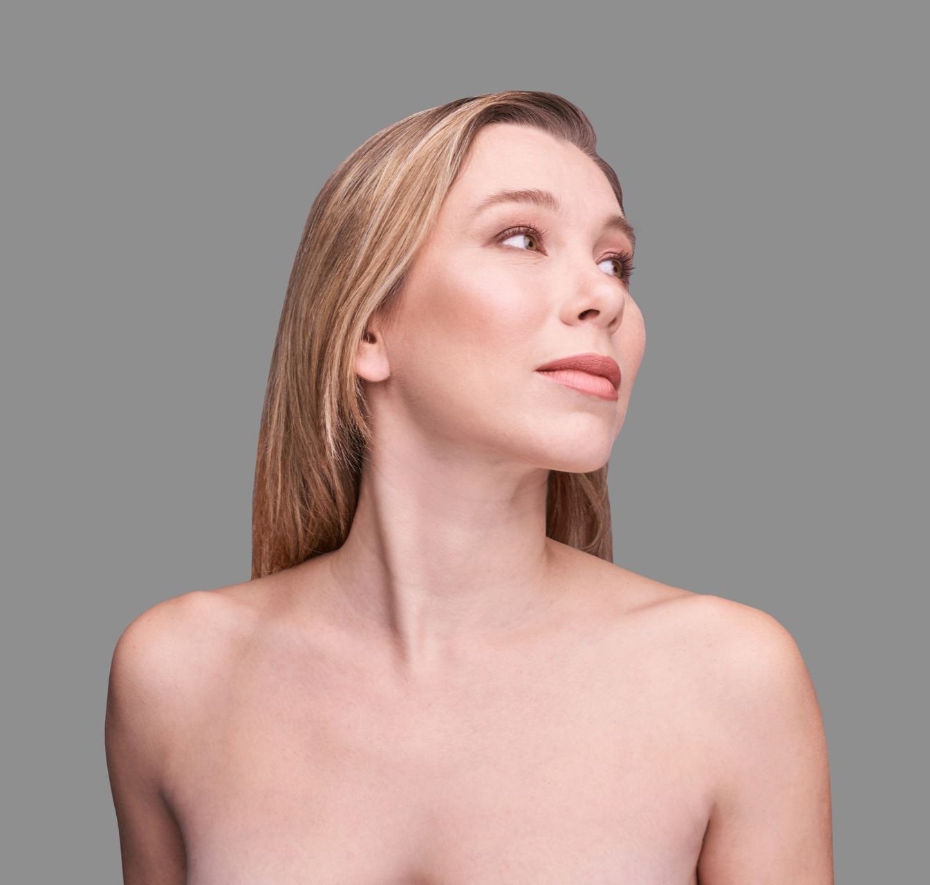 Woman with blonde hair looks to the right against a gray background; bare shoulders.