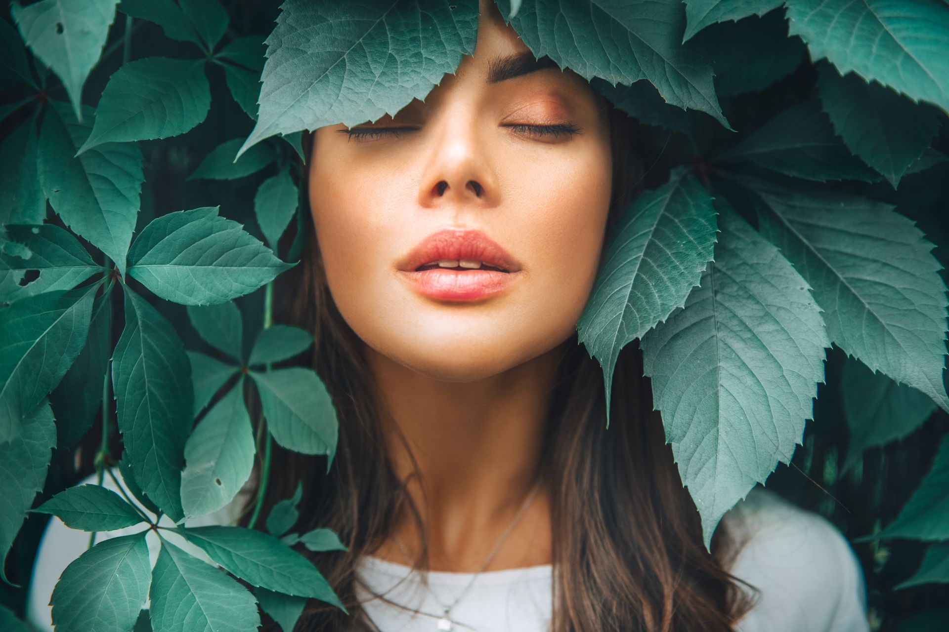 A woman is covering her face with green leaves.