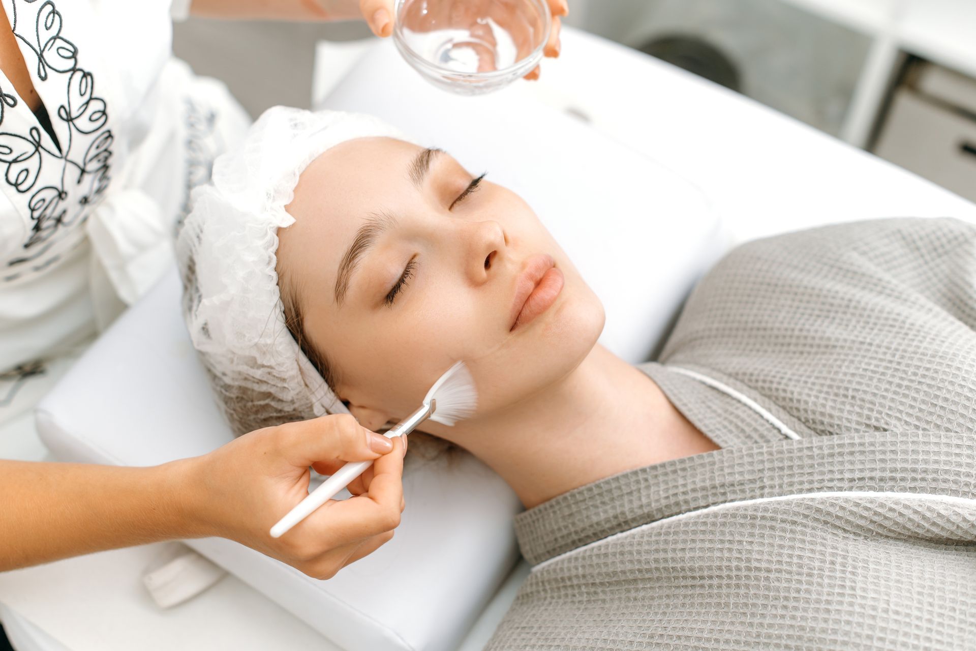 Person receiving facial treatment: a professional applies product to the cheek with a spatula.