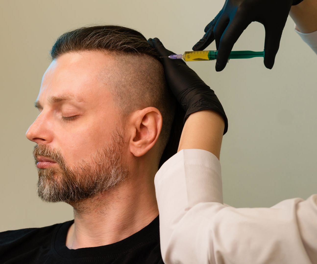 Person receiving injection in the scalp; gloved hand holding syringe.