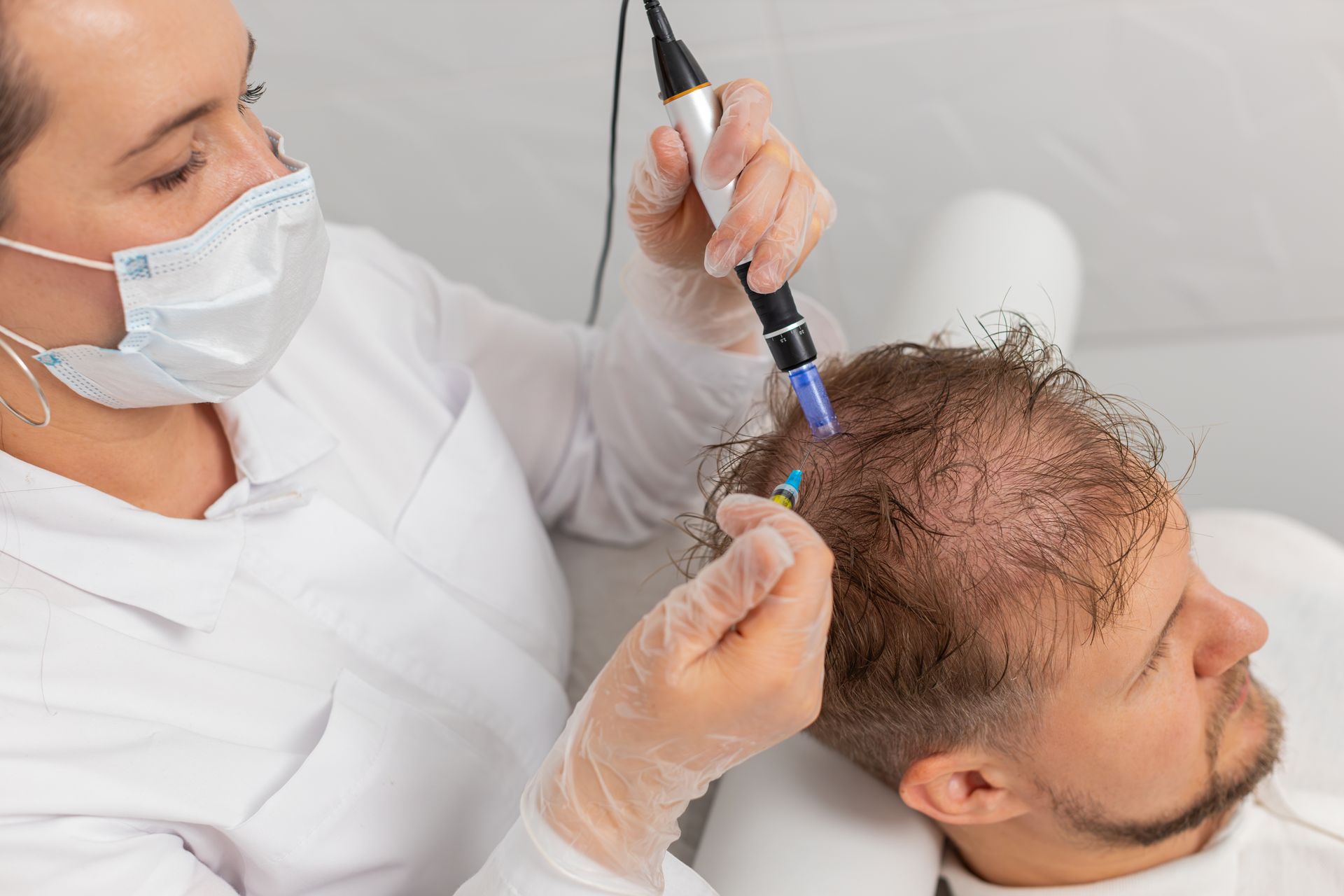 Medical professional administering hair treatment to a patient, using a device on the scalp, in a clinic setting.