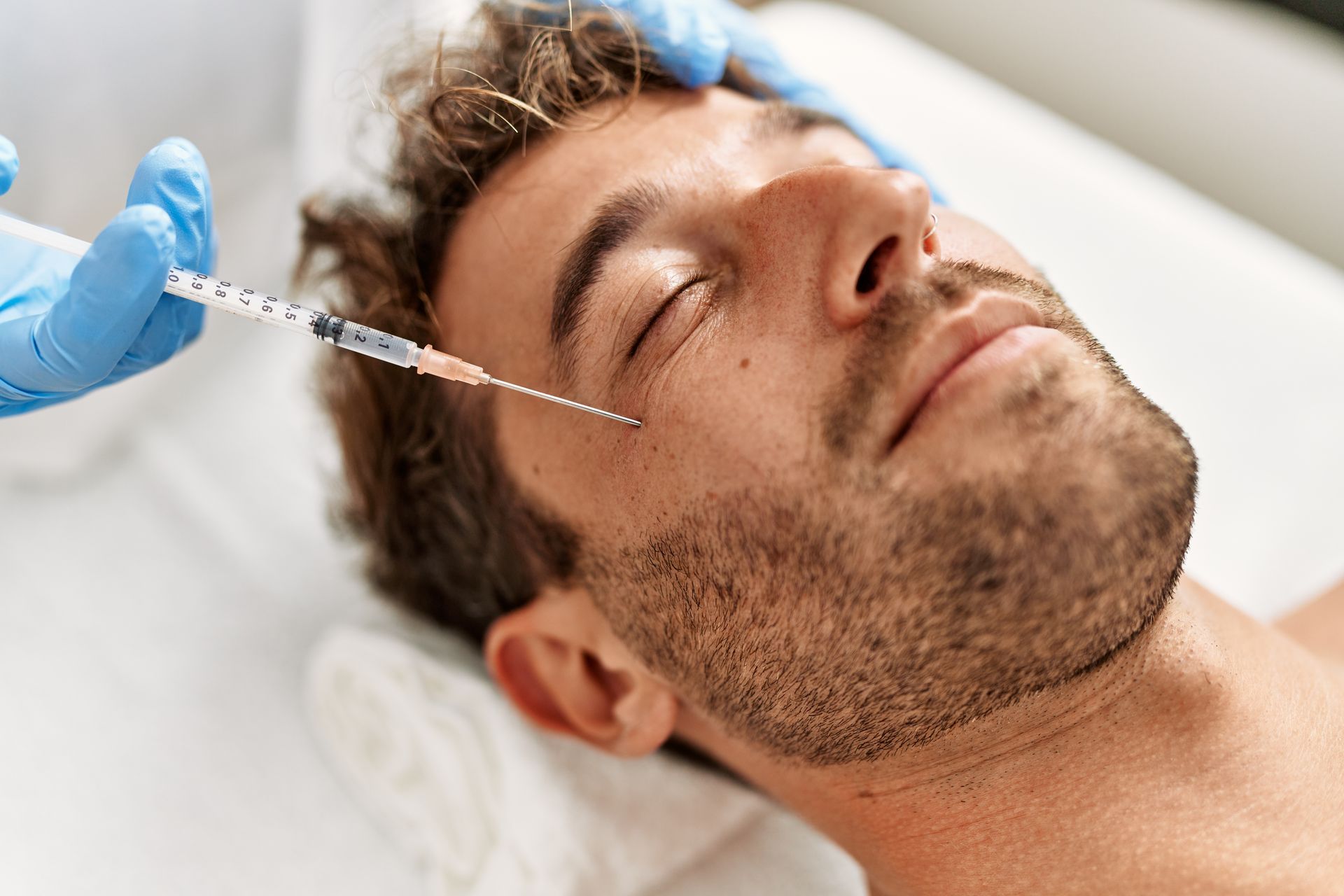 Man receiving facial injection with needle in cheek area. Medical setting, blue gloves.