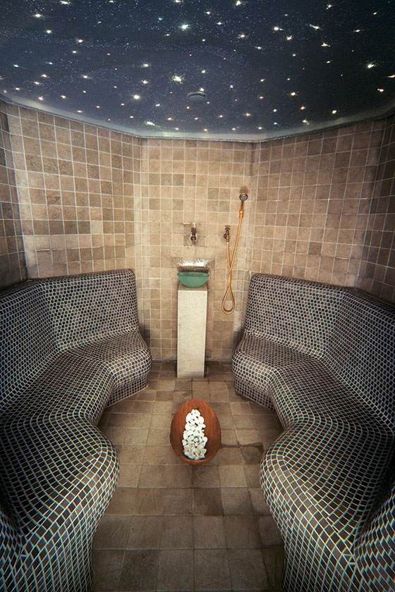 Petite salle de spa carrelée avec deux banquettes en mosaïque, un piédestal central et un plafond étoilé.