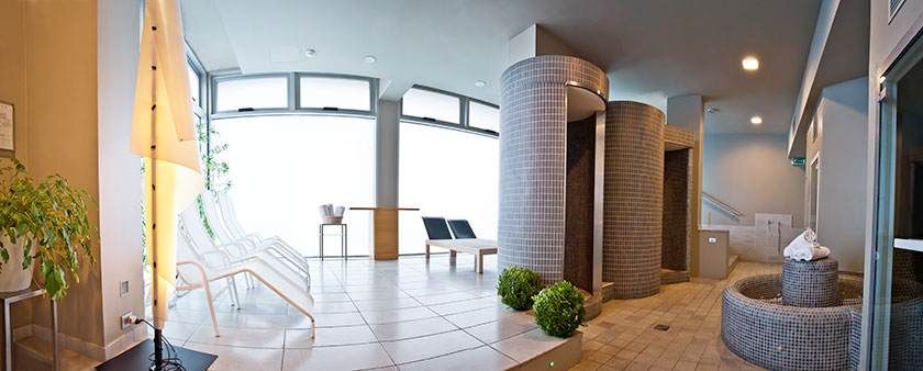 Hall d'entrée d'un immeuble moderne avec sol carrelé, colonnes cylindriques, chaises, plantes et éclairage chaleureux