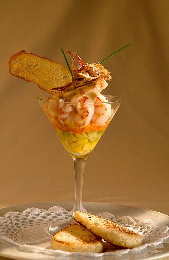 Cocktail de crevettes servi dans un verre à martini, garni d'un gressin et accompagné de tranches de pain grillé