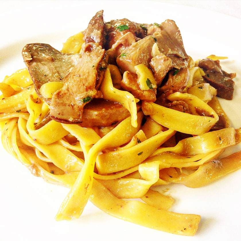 Pâtes avec de la viande émincée dans une sauce jaune crémeuse, servies dans une assiette blanche.