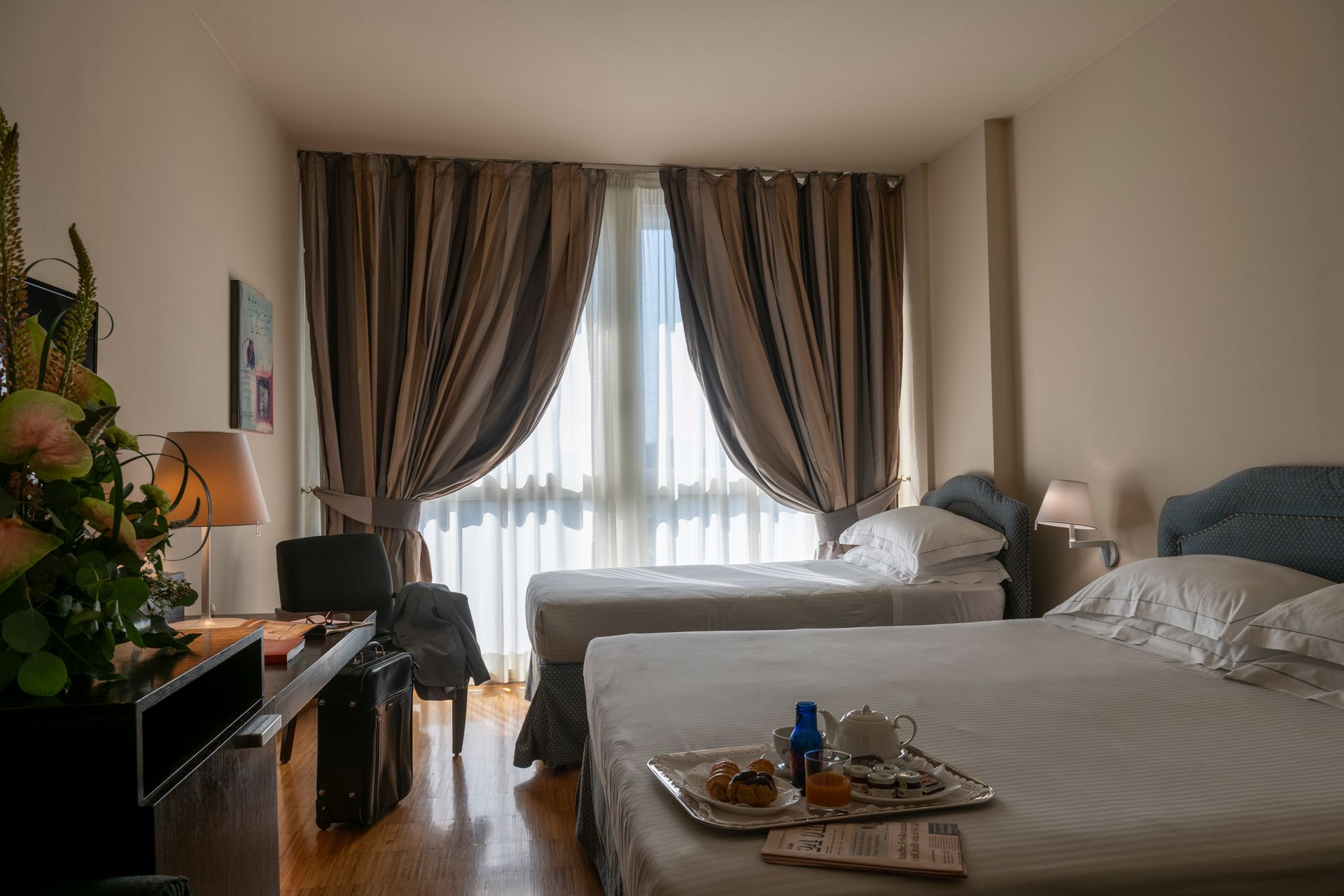 Chambre d'hôtel avec deux lits défaits, une fenêtre avec des rideaux et une petite table près de la télévision.