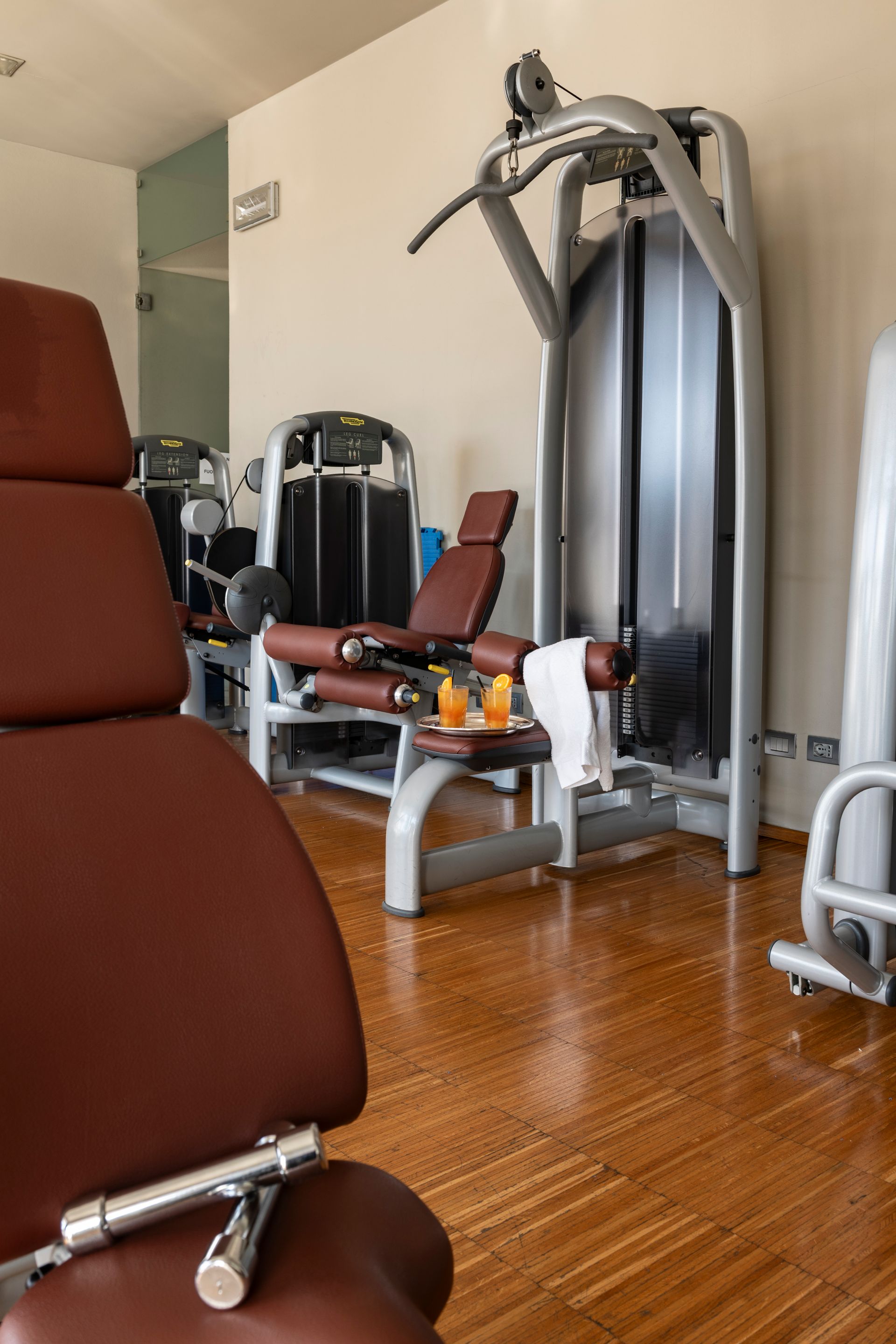 Salle de gym avec sièges rouges pour appareils de musculation et machine à câbles argentée sur parquet.