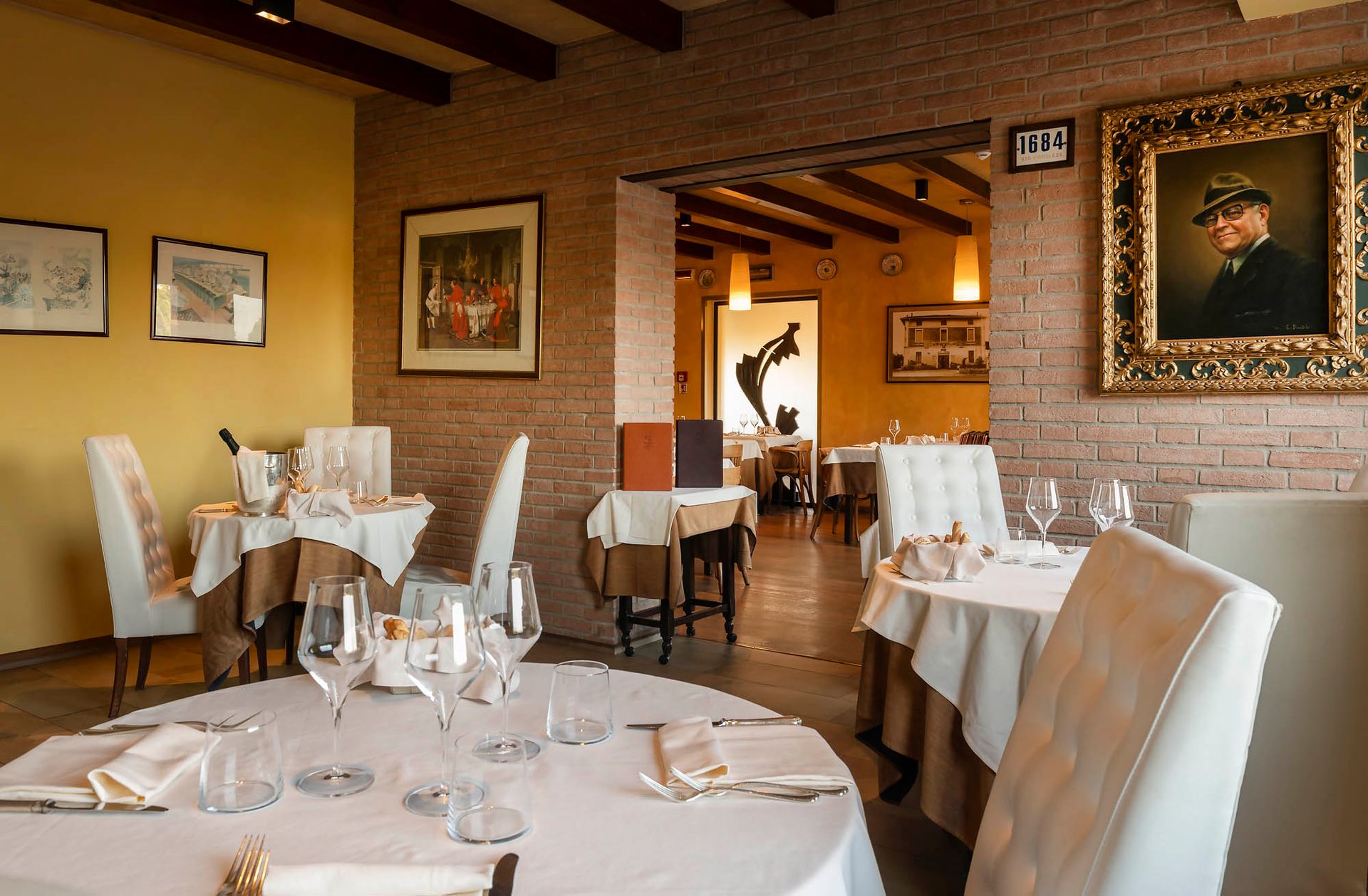 Salle à manger élégante d'un restaurant avec tables dressées, chaises blanches, murs jaune chaud et œuvres d'art encadrées