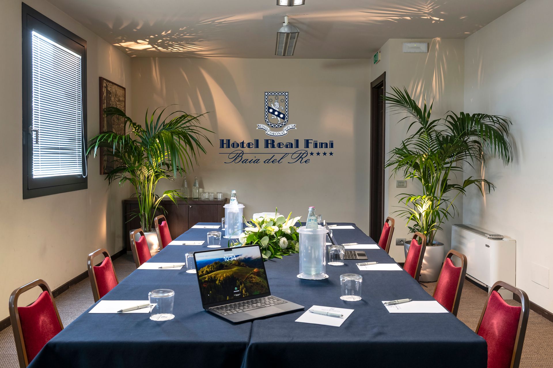 Salle de réunion de l'hôtel Neal Farm avec une longue table, une nappe bleue, des chaises, des plantes et un logo mural