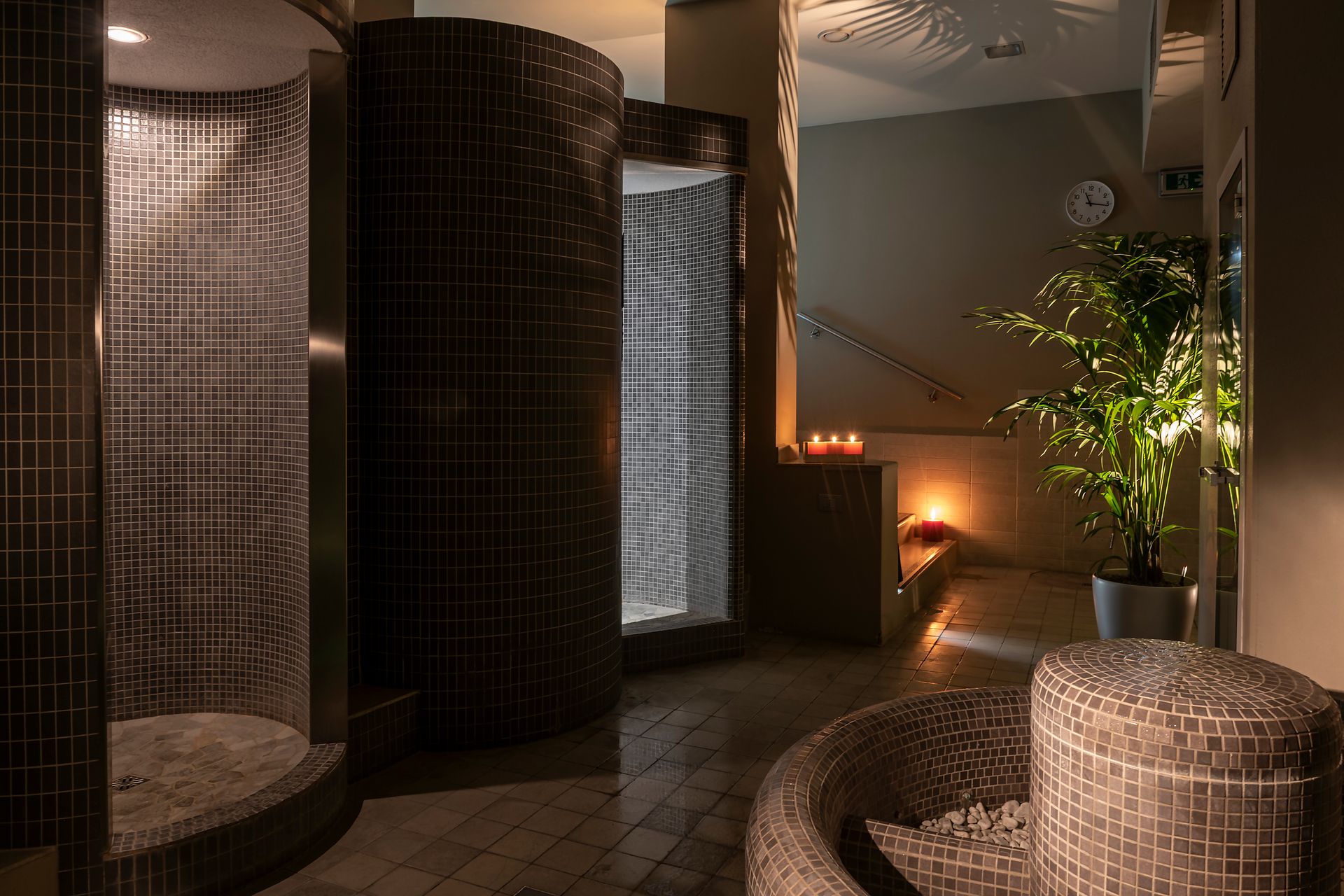 Salon spa tamisé avec fauteuils en osier, colonnes en mosaïque, éclairage chaleureux et plante en pot