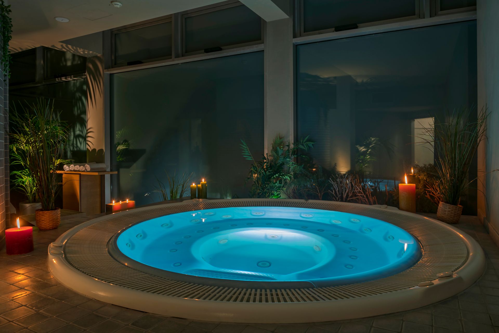 Spa intérieur avec un bain à remous bleu lumineux, des bougies et des plantes la nuit