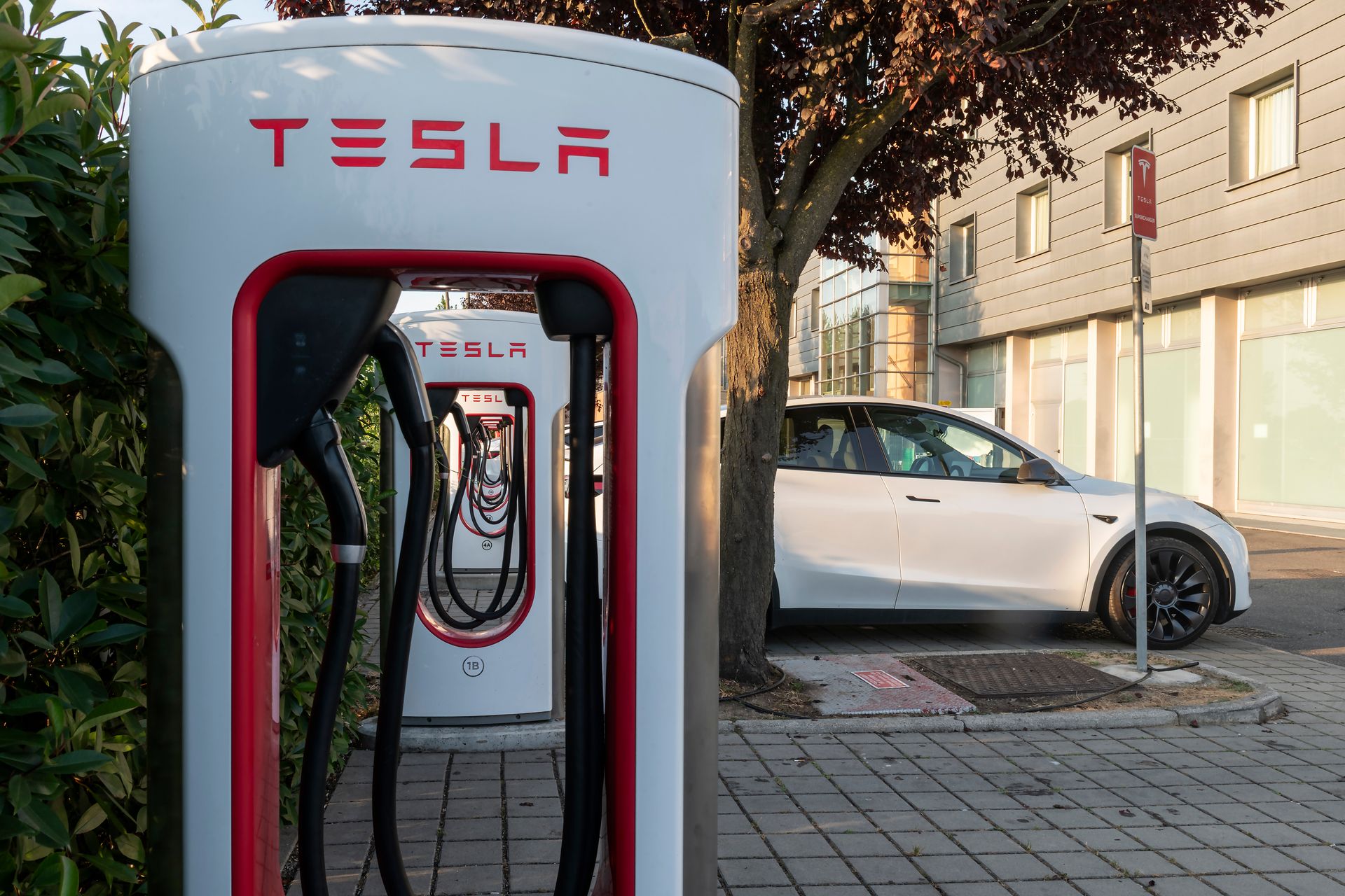 Station de Superchargeur Tesla avec une voiture blanche garée à côté, dans une rue