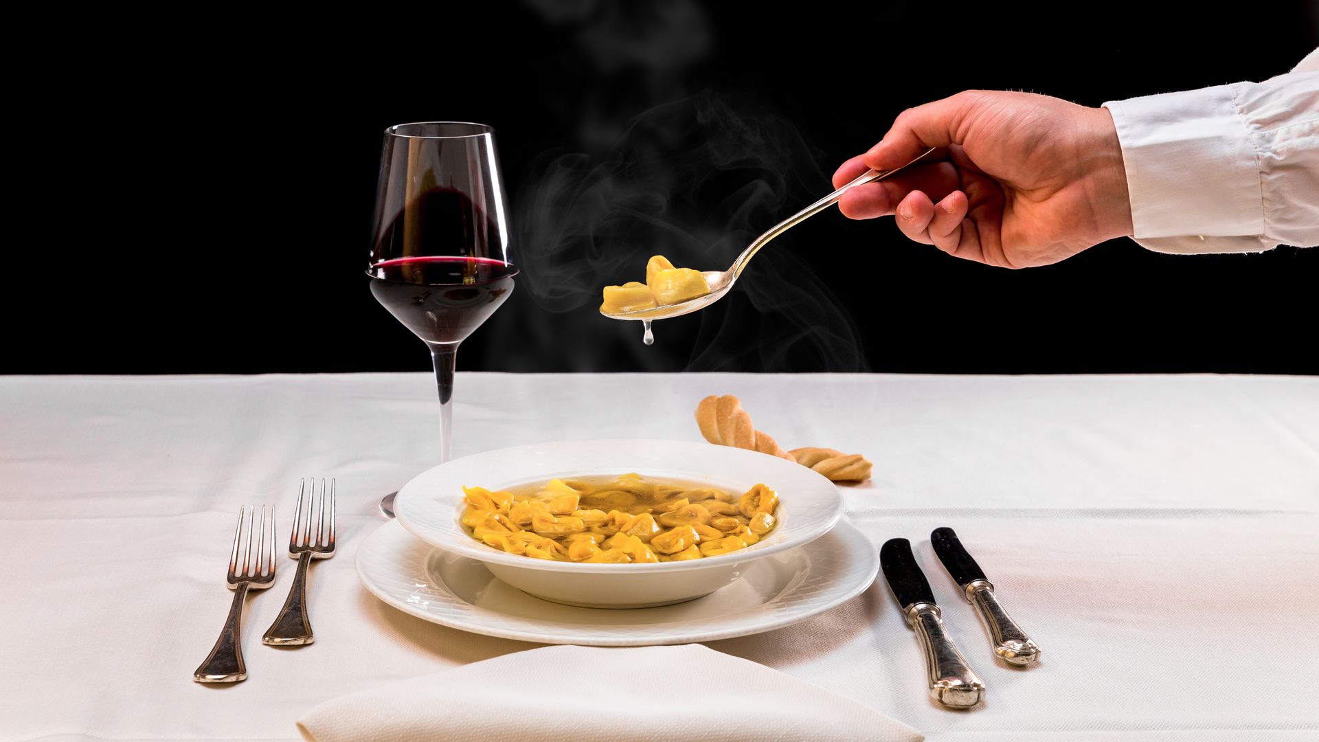 Servir des tortellini à la main, puis dresser une assiette sur une table blanche, accompagnée d'un verre de vin rouge.
