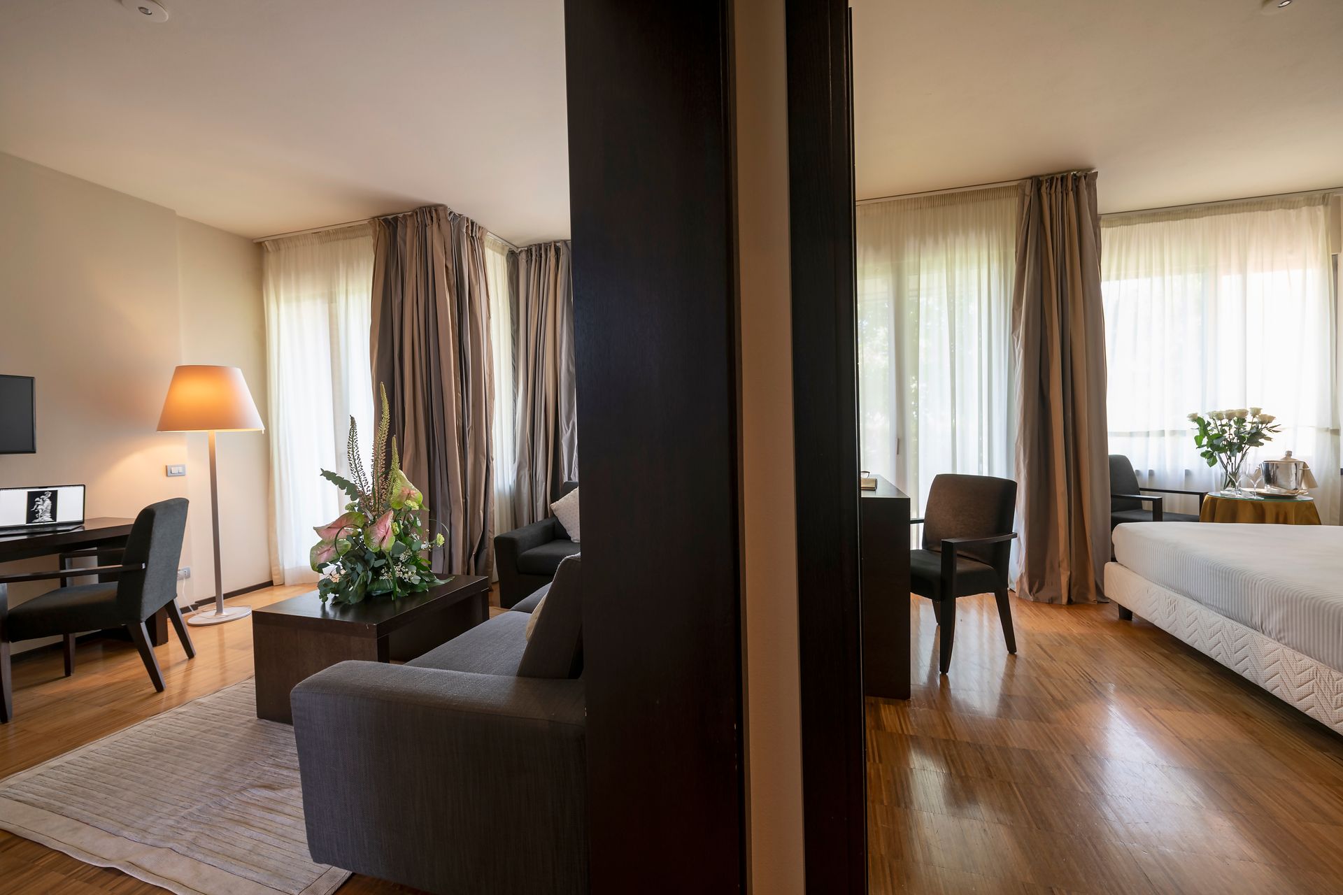 Chambre et bureau modernes avec parquet chaleureux, grandes fenêtres et rideaux, séparés par une cloison centrale.