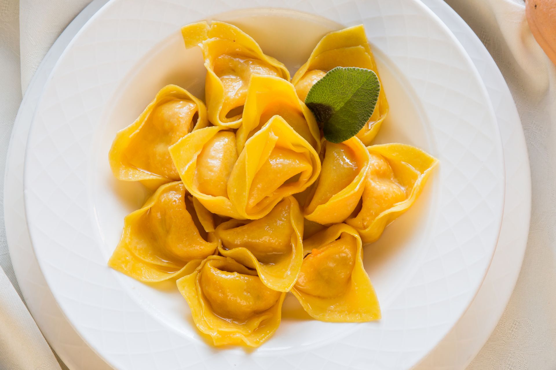 Assiette de tortellini garnie d'une feuille de basilic, servie dans un plat blanc.