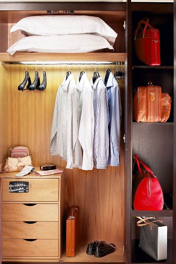 Placard ouvert avec chemises suspendues, étagères, chaussures et sacs à main dans une penderie bien rangée.