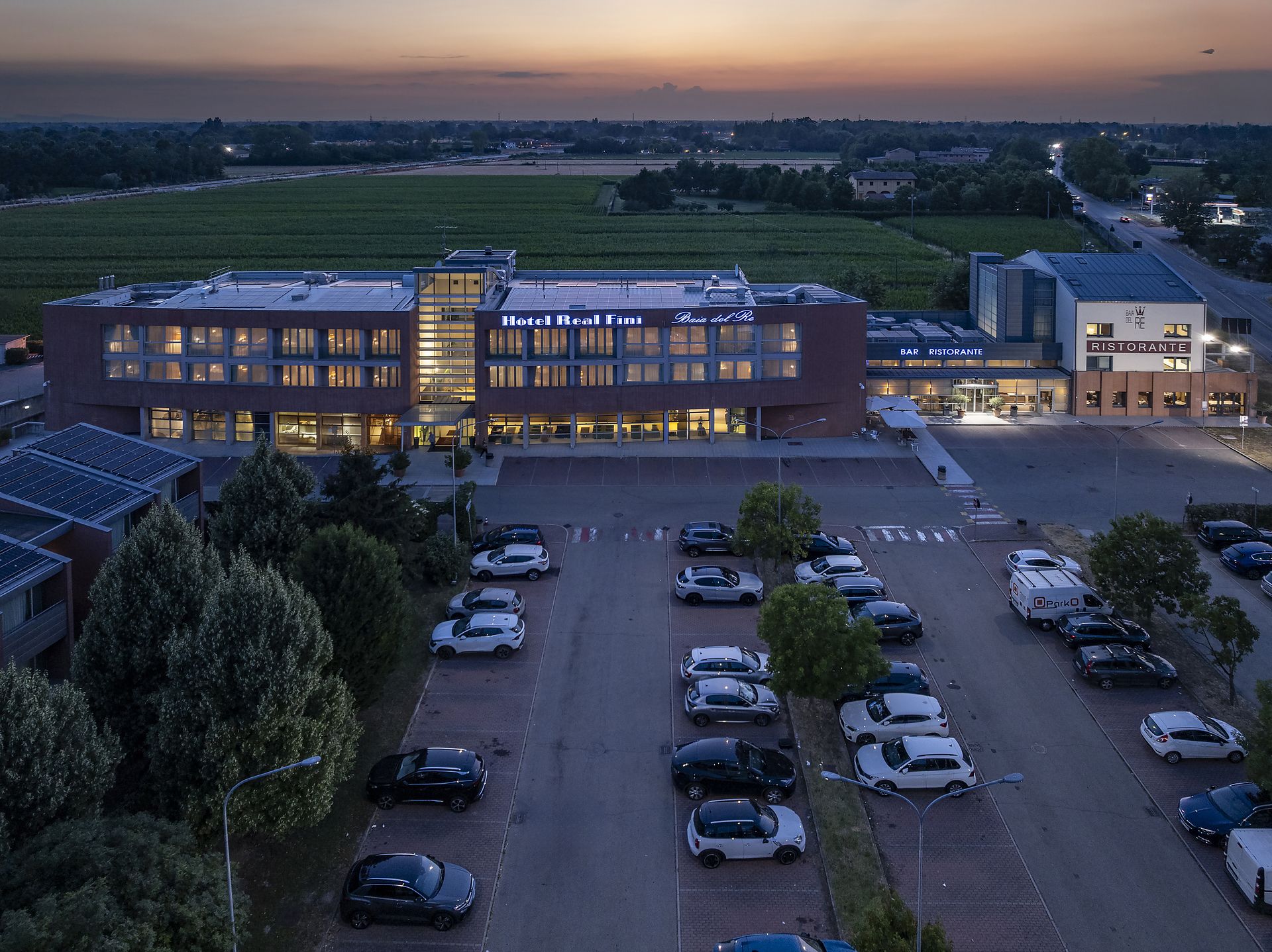 Vue aérienne au crépuscule d'Hotel Real Fini Baia del Re et d'un parking en bordure d'une route et de verdure.