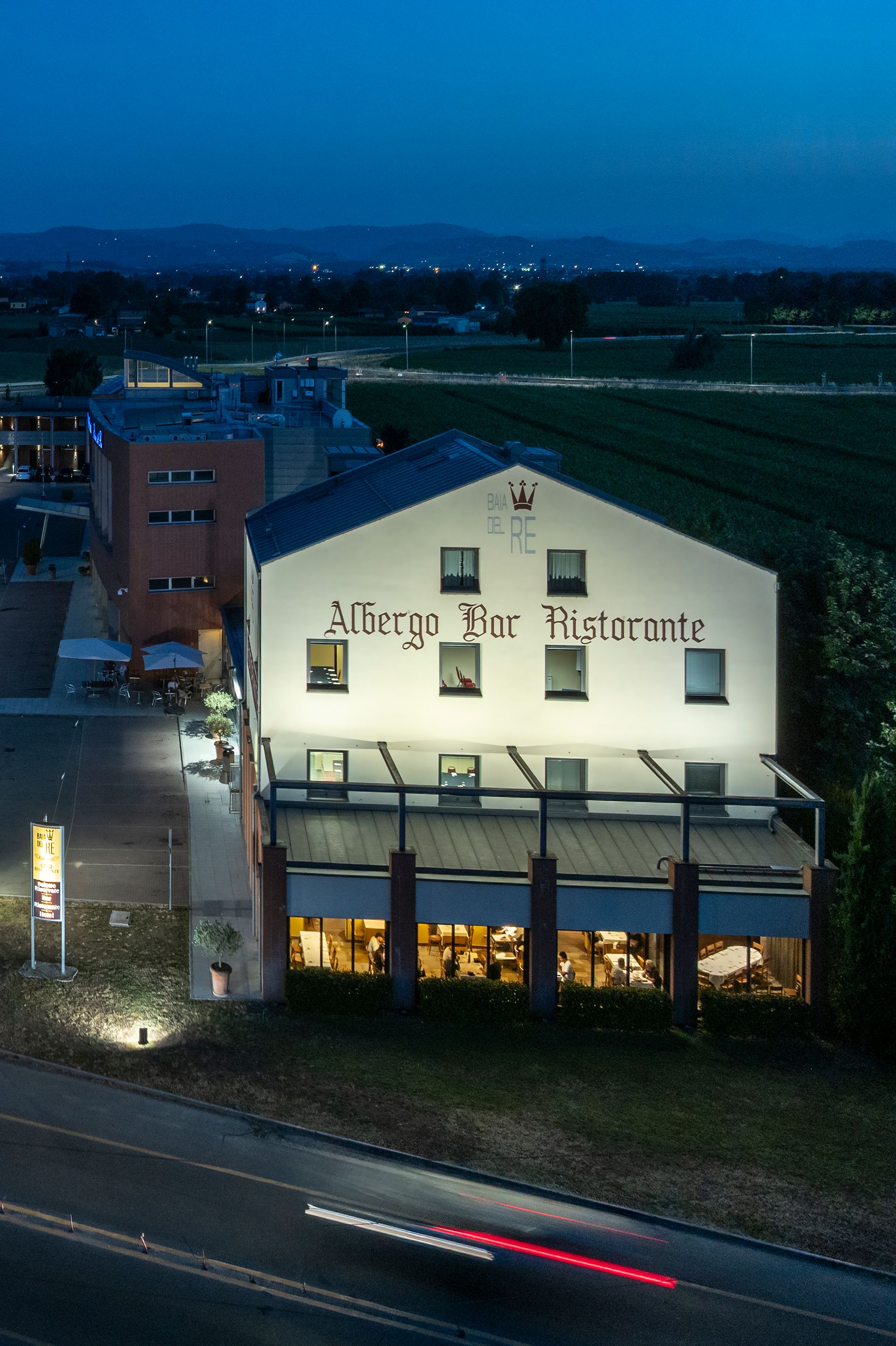 Bâtiment d'un restaurant illuminé au crépuscule, en bordure de route, avec des voitures qui passent au premier plan.