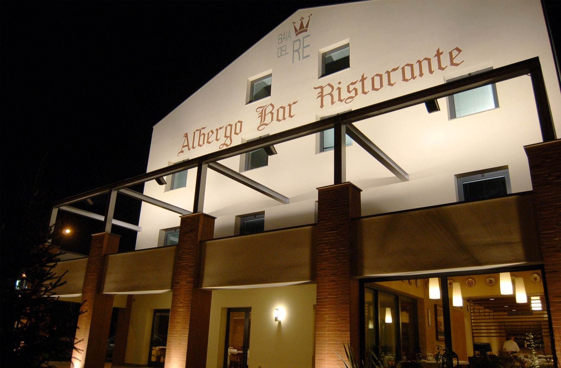 Vue nocturne d'Hotel Real Fini Baia del Re abritant un bar-restaurant, avec une enseigne blanche et une façade en briques.