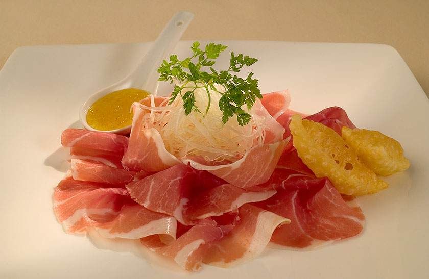 Entrée de prosciutto et melon sur une assiette blanche, garnie d'herbes et de quartiers de citron.