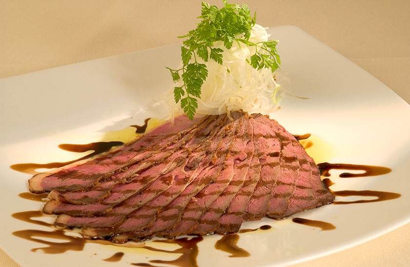 Tranches de rôti de bœuf sur une assiette blanche, arrosées de sauce et garnies d'herbes et de chou.